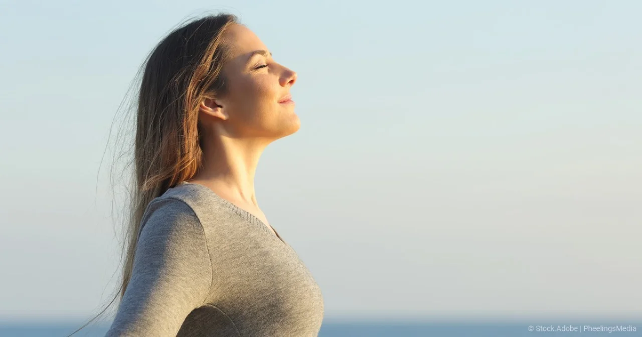 Frau atmet tief ein und hält Gesicht in Richtung Sonne