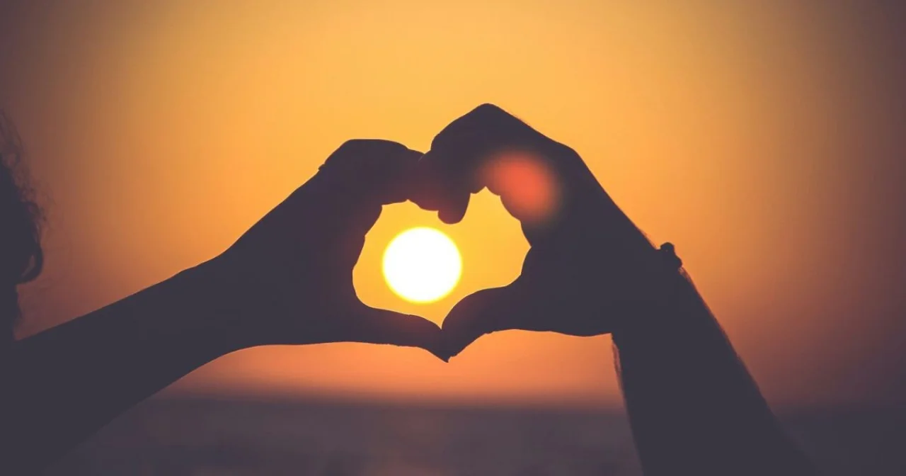 Zwei Hände, die um einen Sonnenuntergang ein Herz formen