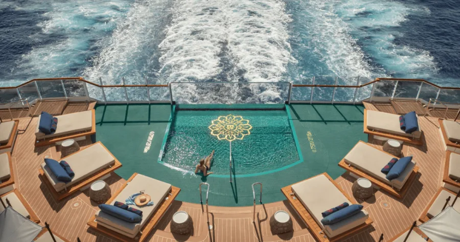 Alleinreisende Frau im Astern Pool am Heck einees Explora Kreuzfahrtschiffes blickt aufs Meer