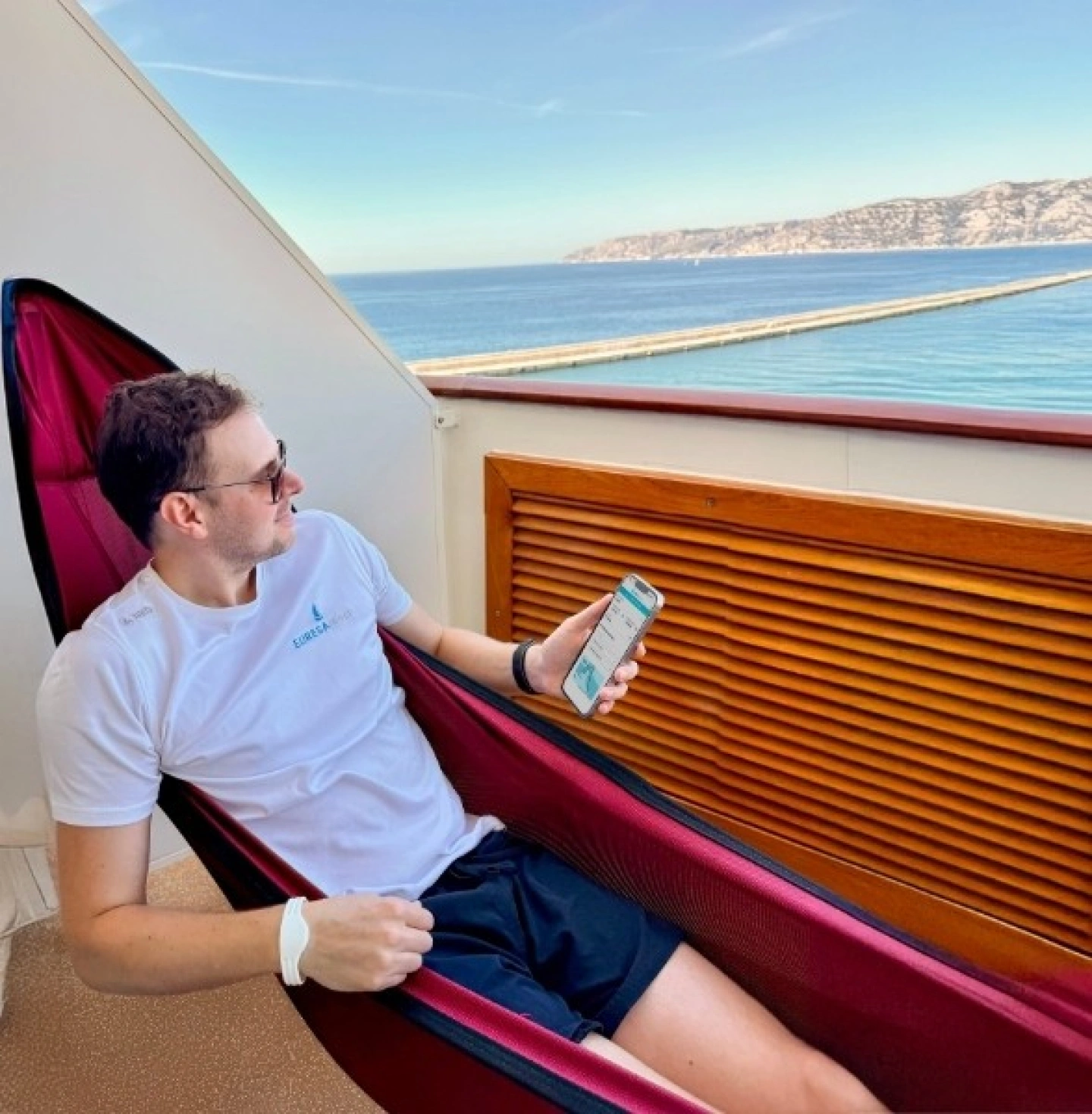 Johannes in Hängematte auf Kabinenbalkon mit EURESAreisen Reisesuche auf Handy
