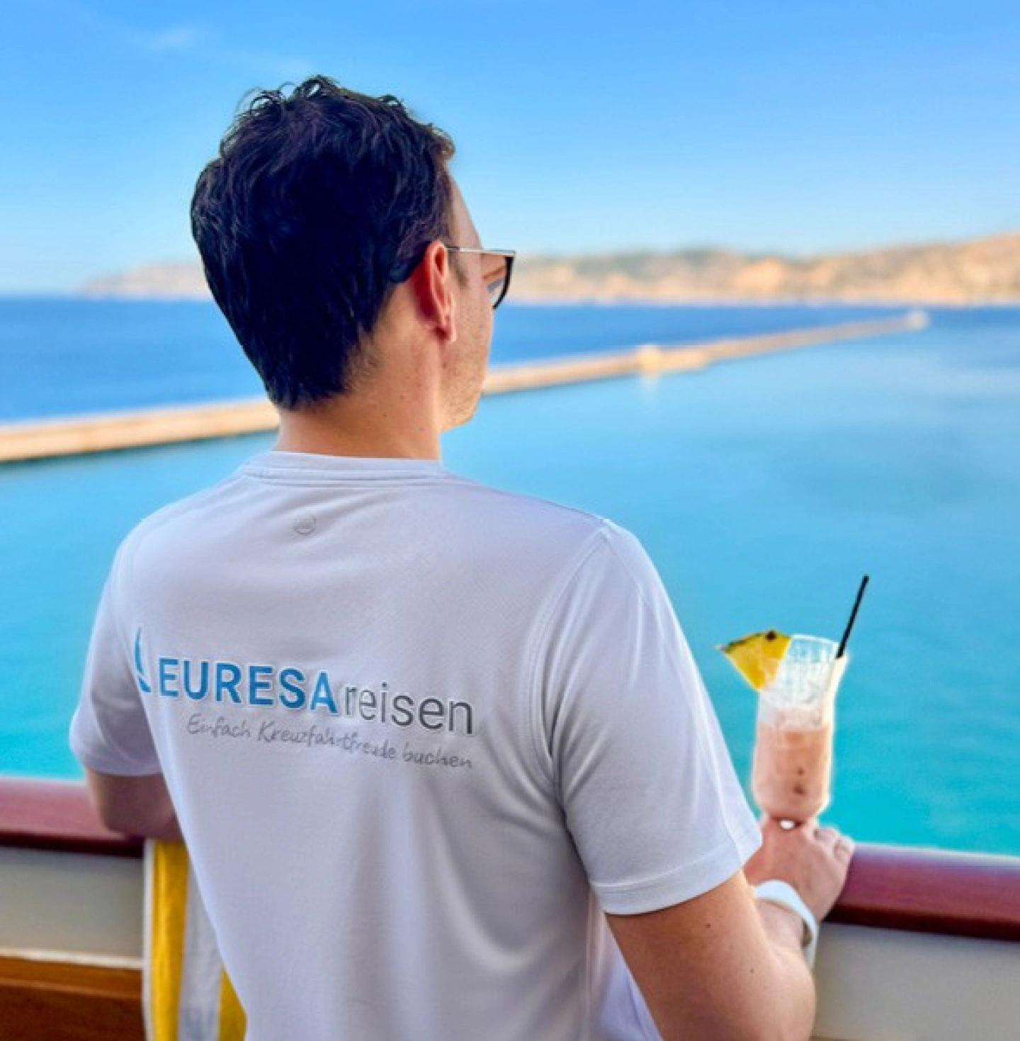 EURESAreisen Geschäftsführer Johannes genießt den Meerblick mit einem Cocktail in der Hand auf dem Kabinenbalkon an der Reling